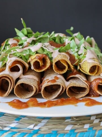 A side shot of vegan Rolled Tacos drizzled with hot sauce