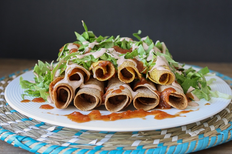 A side shot of vegan Rolled Tacos drizzled with hot sauce