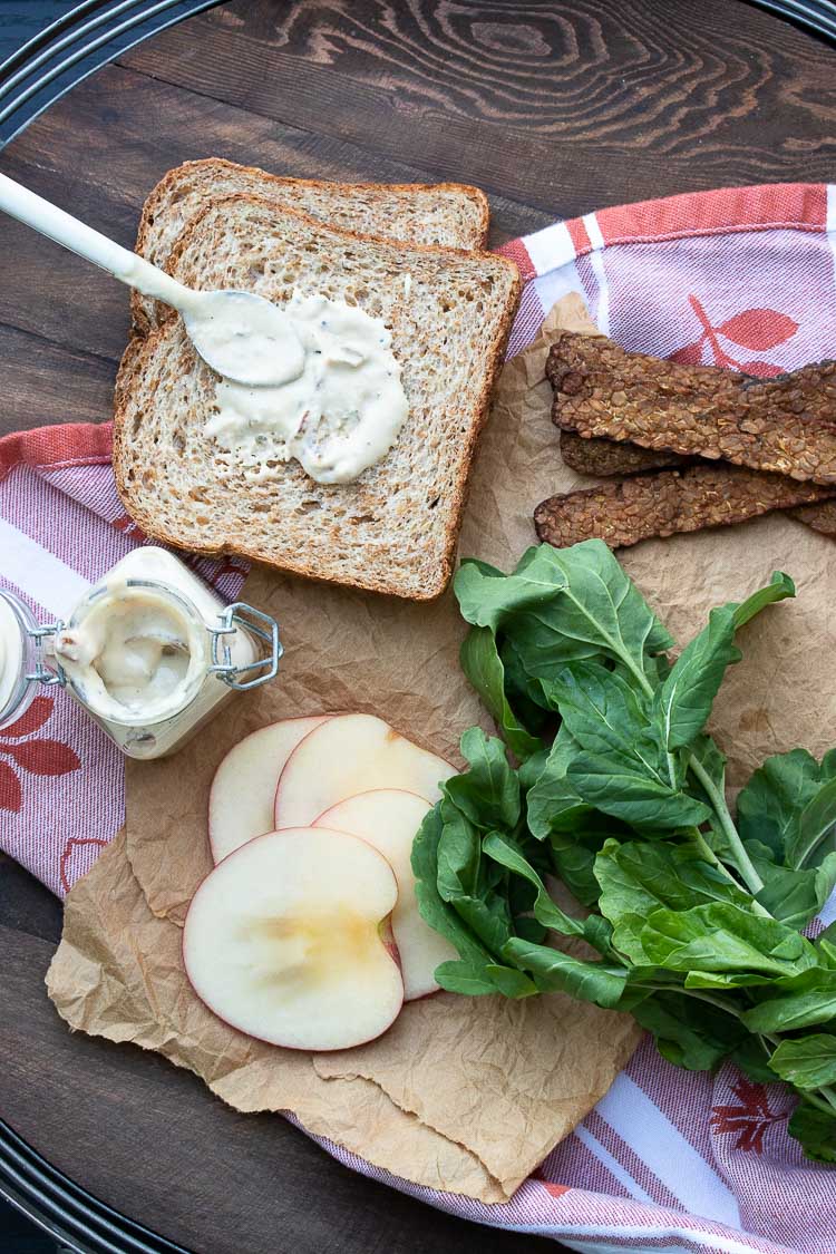 Top view of aioli being spread onto a slice of bread surrounded sandwich ingredients