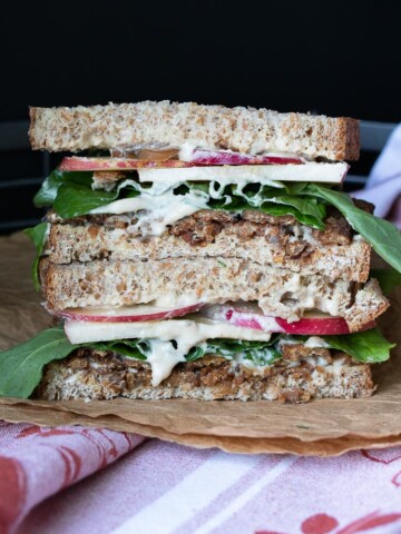 Front view of vegan tempeh bacon, apple, arugula sandwich on brown crumpled paper