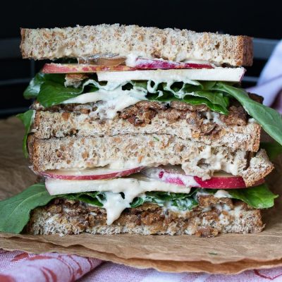 Front view of vegan tempeh bacon, apple, arugula sandwich on brown crumpled paper