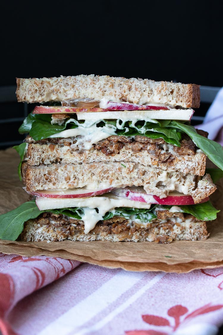 Front view of vegan tempeh bacon, apple, arugula sandwich on brown crumpled paper