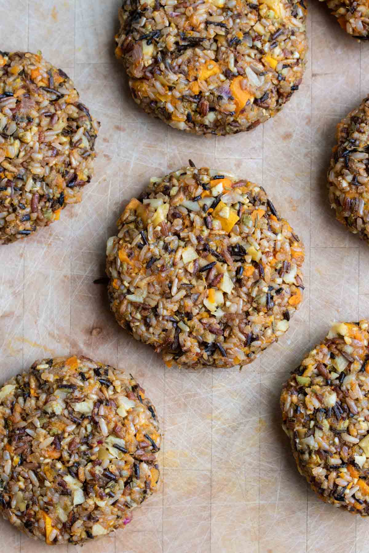 Raw butternut squash and wild rice burger patties on a wooden surface.