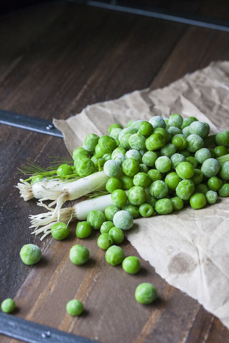 Frozen peas, scallions and dill piled on brown parchment paper