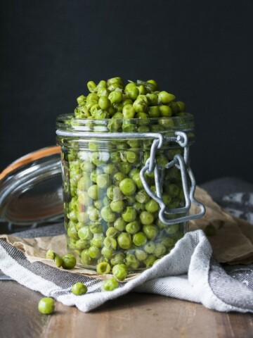 Cooked peas with scallions and dill piled high in a glass jar