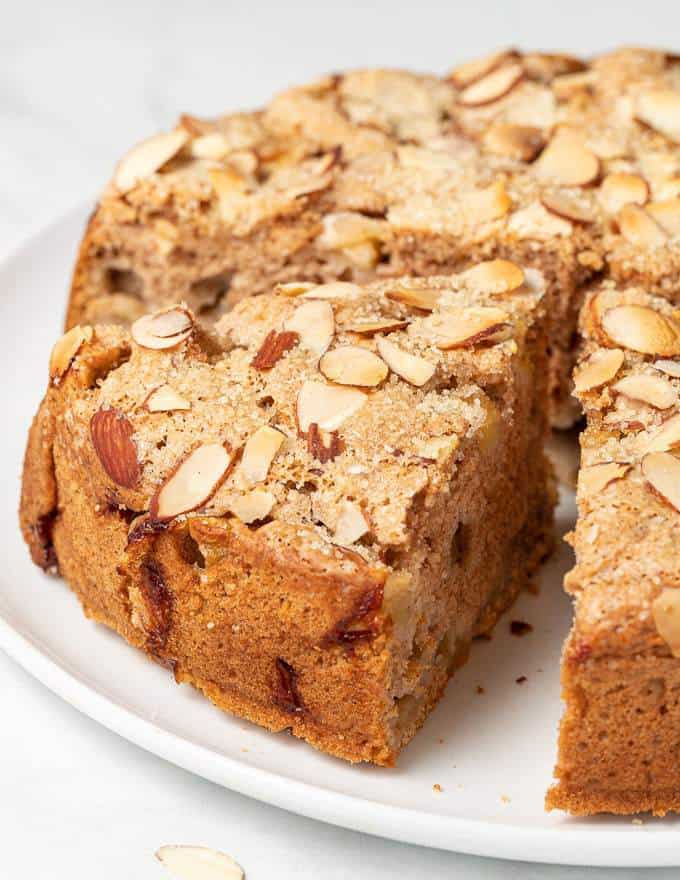 A cut almond and apple cake on a white plate