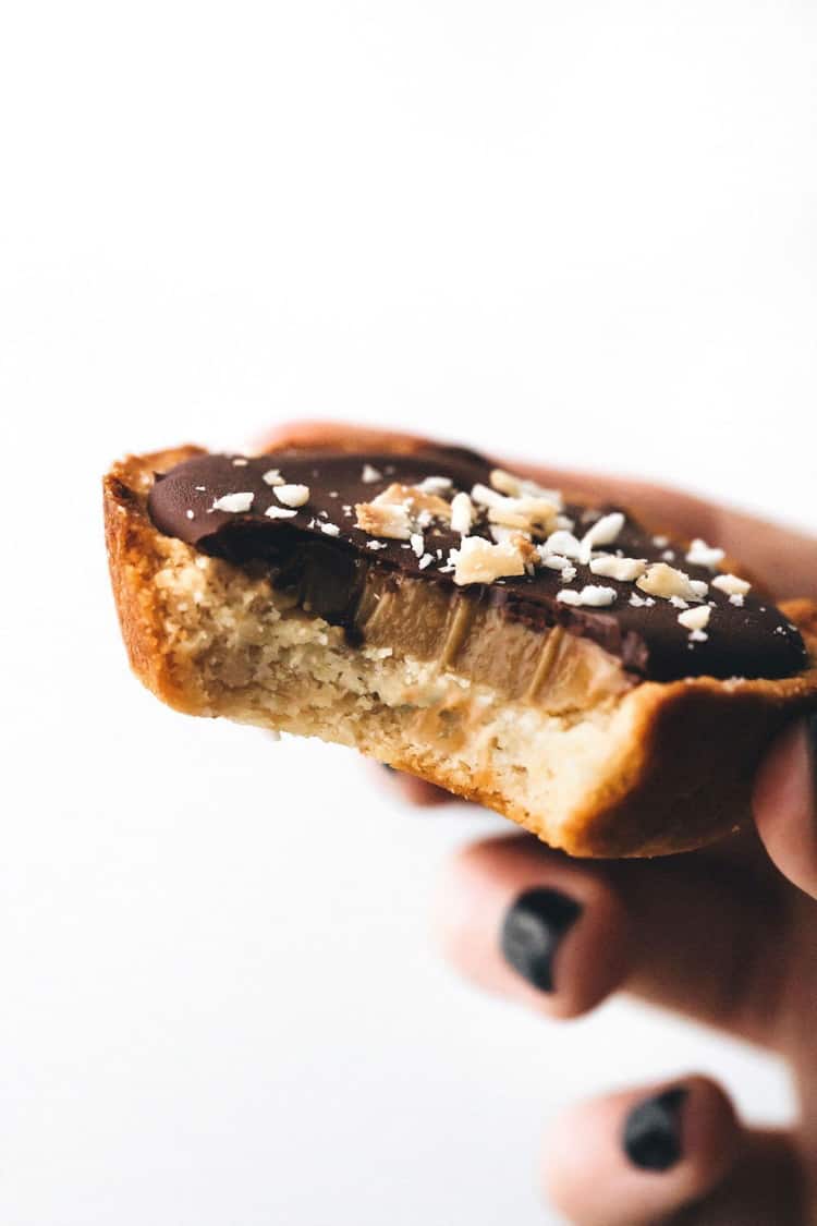 Hand holding a shortbread cookie with caramel and chocolate on top