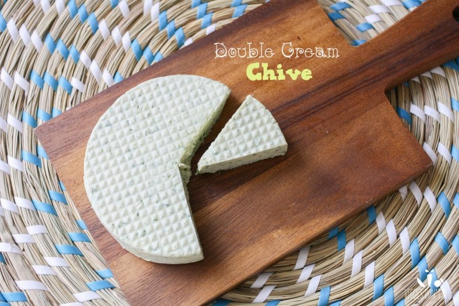 A photo of a round Miyoko's Creamery Vegan Cheese with a slice cut out sitting on a wooden board Miyoko's Creamery Vegan Cheese