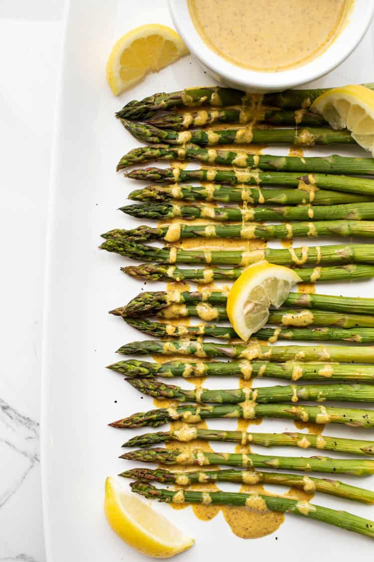 Asparagus on a white platter with lemon cream sauce drizzled over