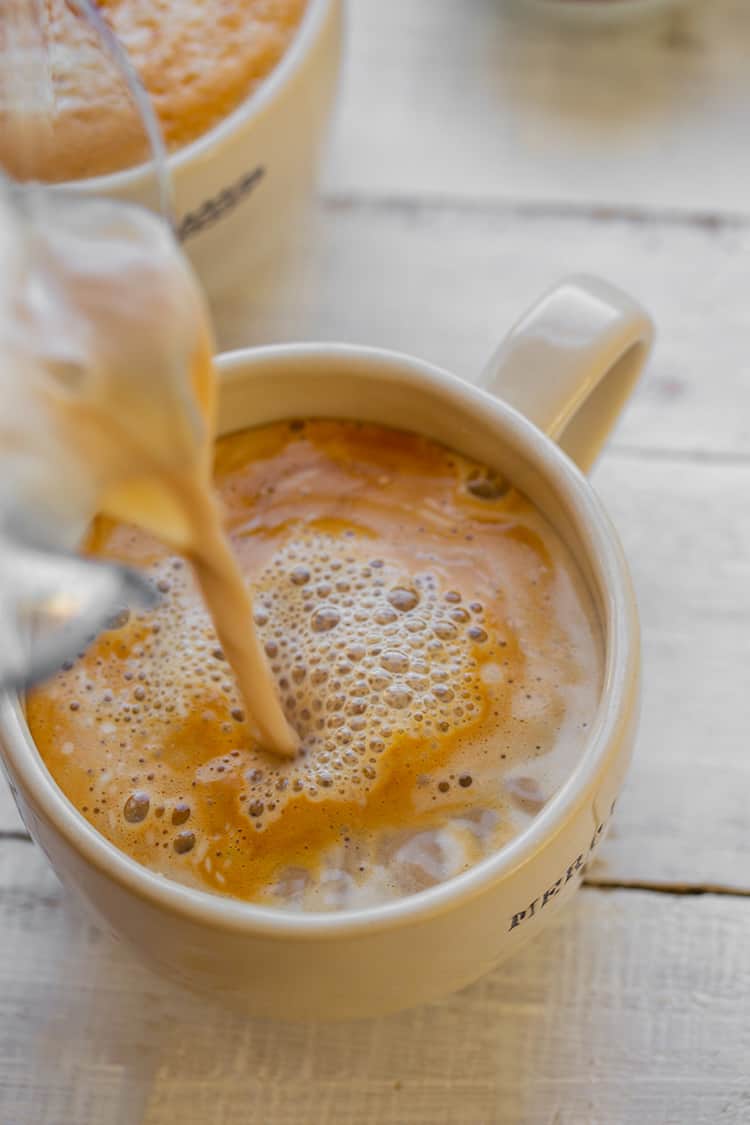 A cinnamon latte being poured into a mug