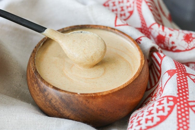 A spoons cooping up some Pistachio buffalo cream sauce from a wooden bowl