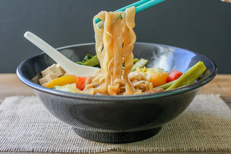A photo of chopsticks picking up noodles from a soup bowl
