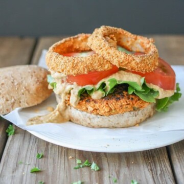 Buffalo chickpea burger topped with baked cornmeal and pepita crusted onion rings and pistachio buffalo cream