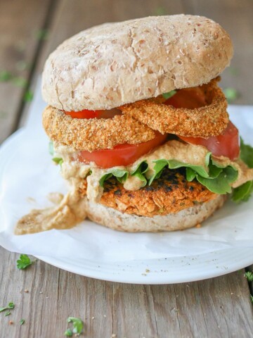 Buffalo chickpea burgers on a bun with onion rings and sauce on a white plate