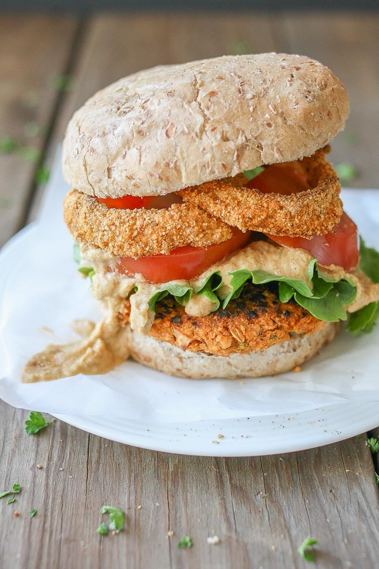 Buffalo chickpea burgers on a bun with onion rings and sauce