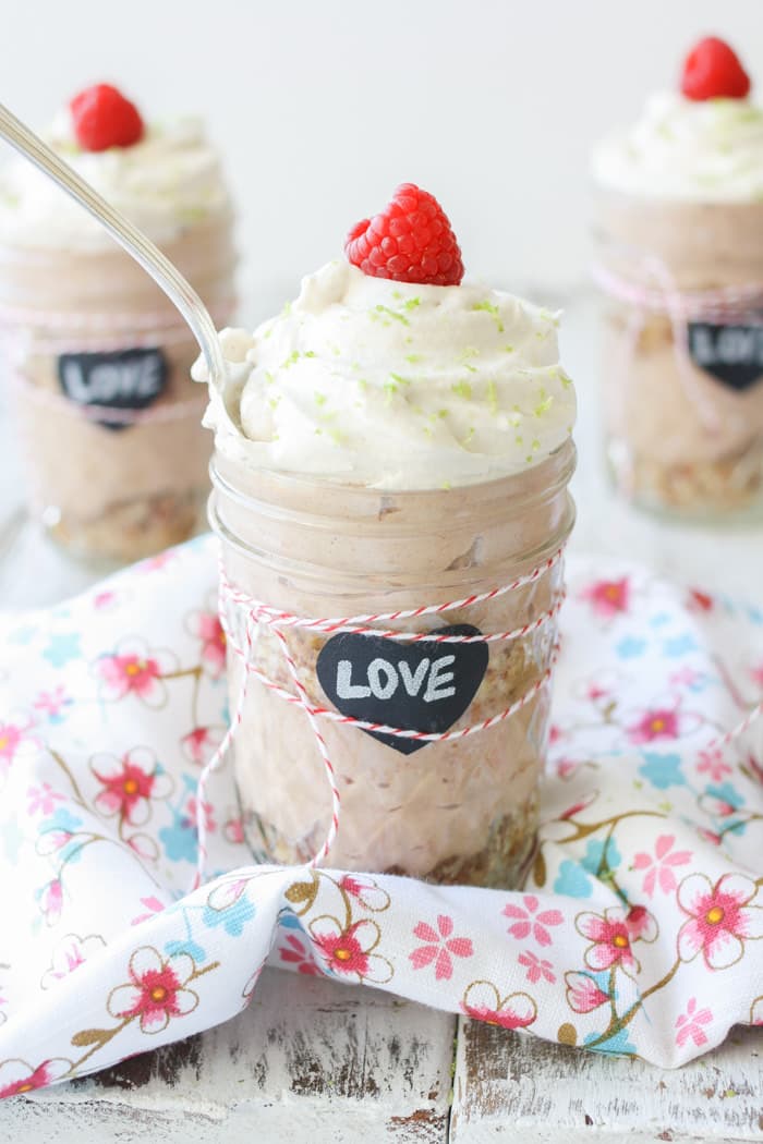 Key lime raspberry pudding parfait in glass jars sitting on a wooden surface