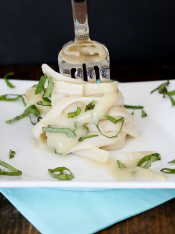 A fork twisting some tagliatelle on a plate with garlic alfredo sauce