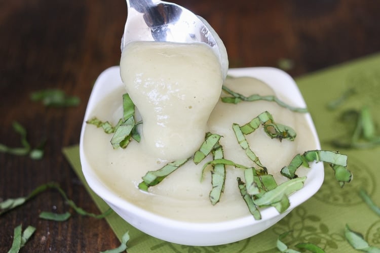 A close up of thick and creamy garlic alfredo sauce in a white bowl with a spoon