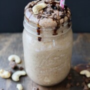 A Salted caramel smoothie topped with cashews and chocolate chips around it sitting on a wooden surface