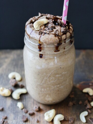 A Salted caramel smoothie topped with cashews and chocolate chips around it sitting on a wooden surface