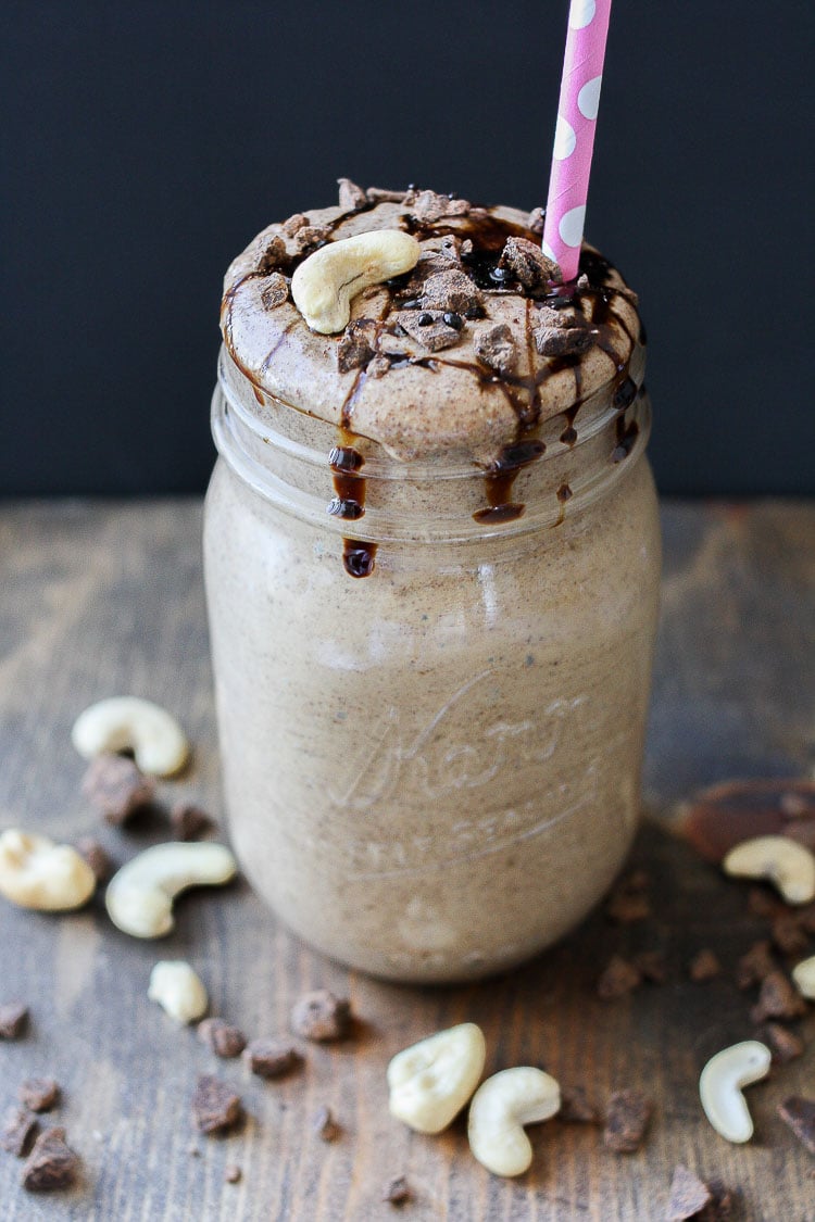 A Salted caramel smoothie topped with cashews and chocolate chips around it sitting on a wooden surface