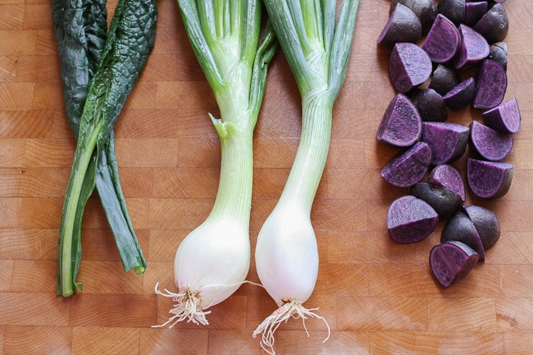 Leeks, chard and purple potatoes on a wooden board used to make a tahini power bowl