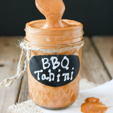 Barbecue tahini sauce in a glass jar sitting on a wooden surface