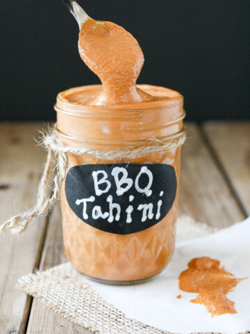 Barbecue tahini sauce in a glass jar sitting on a wooden surface