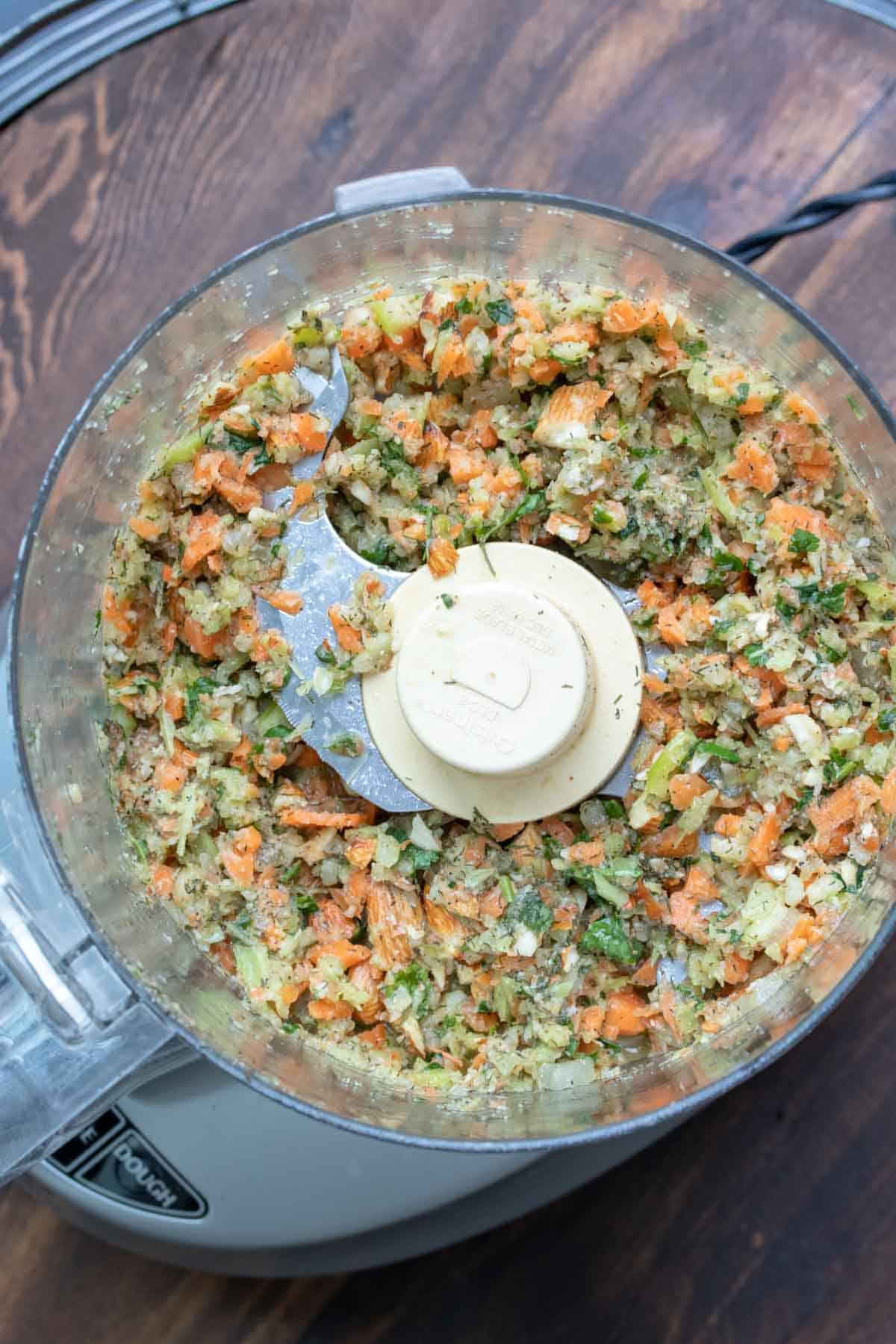 Top view of food processor pulsing chickpeas and veggies.