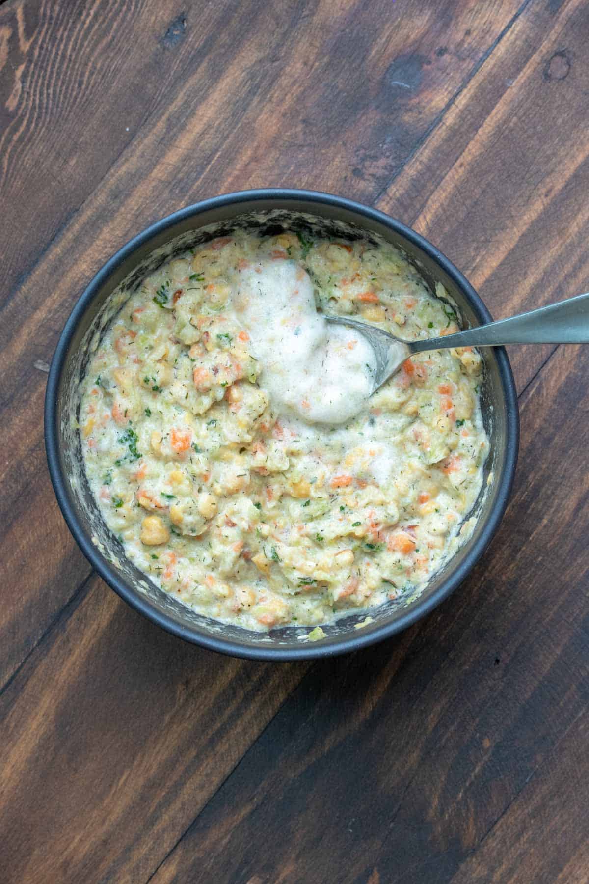 Spoon mixing creamy froth into mashed chickpeas and veggies.