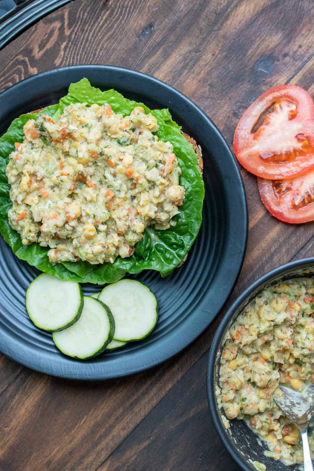 Black plate with mashed chickpea salad on a piece of lettuce on bread.