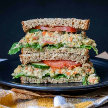 Mashed chickpea salad sandwich with veggies piled on a black plate