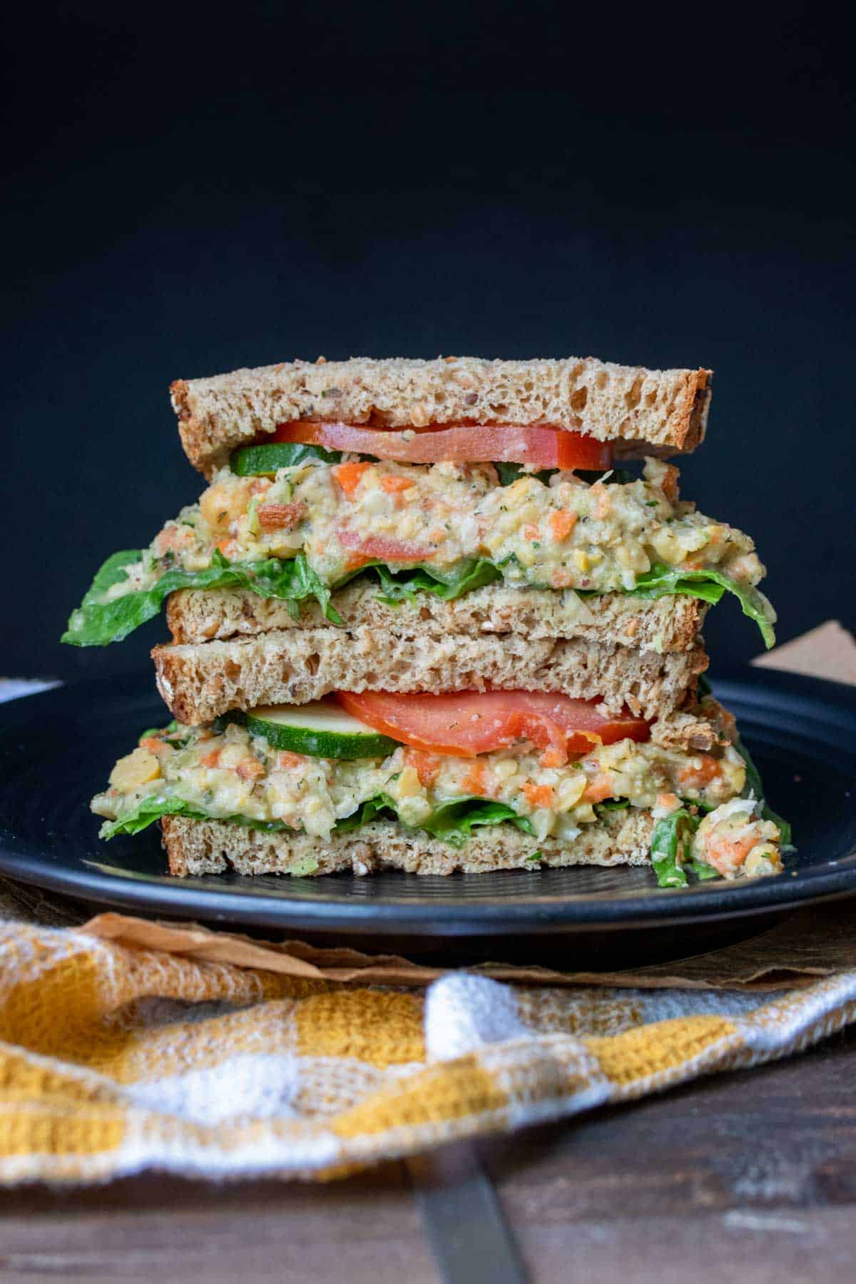 Mashed chickpea salad sandwich with veggies piled on a black plate