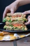 Hands picking up half a mashed chickpea sandwich with veggies