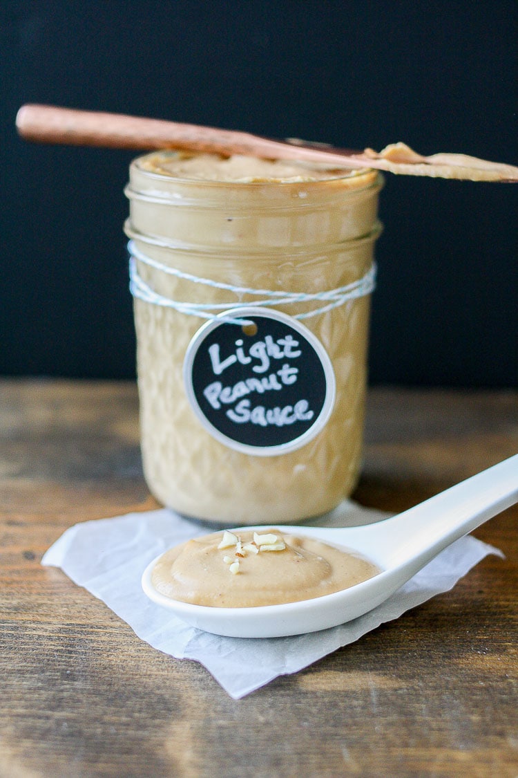 A jar of creamy peanut sauce with a small knife on top and spoon at the side