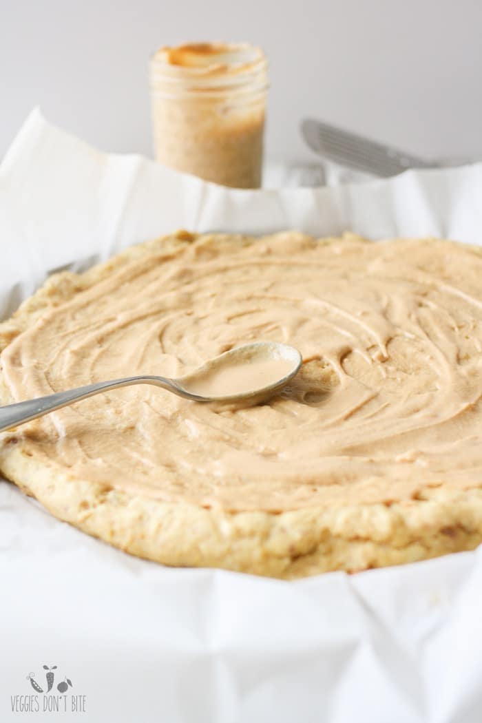 A veggie pizza base getting spread with a peanut sauce