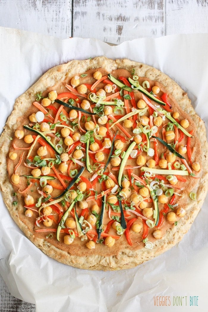 A baked Thai chickpea and veggie pizza on a white wooden surface