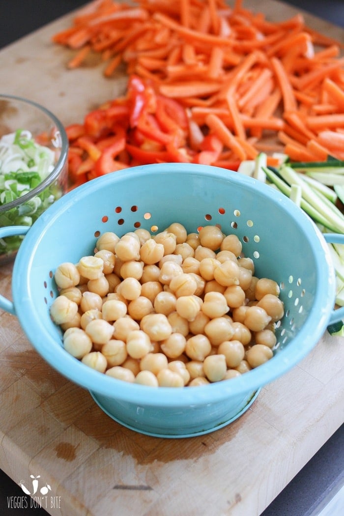 Chickpeas in a blue colander and other chopped vegetables in the background for making a veggie pizza 