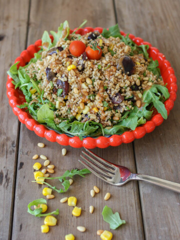 A vegan arugula salad on a white plate with a fork