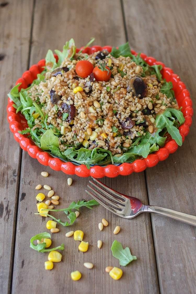 A vegan arugula salad on a white plate with a fork