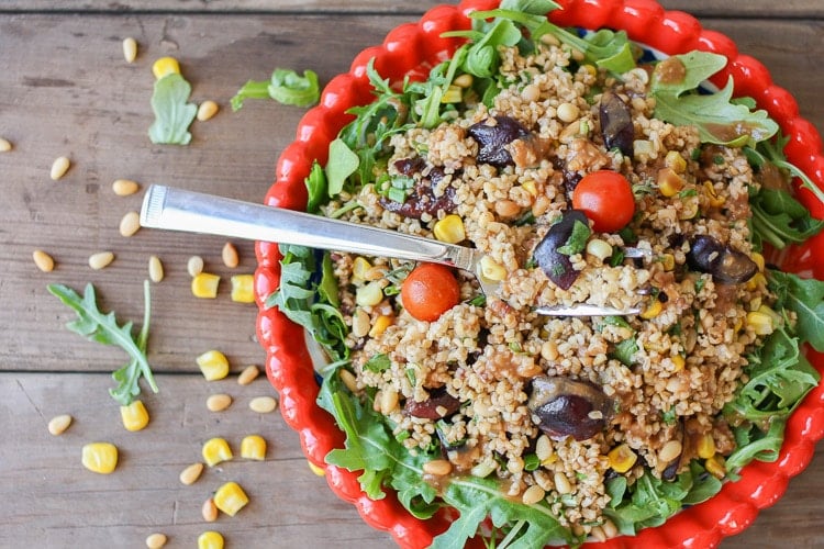 An overhead shot of a vegan arugula salad in a red bowl sitting on a wooden surface