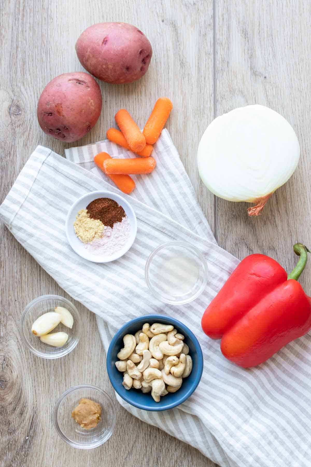 Top view of veggies, cashews, garlic, spices and lemon juice on a wooden surface