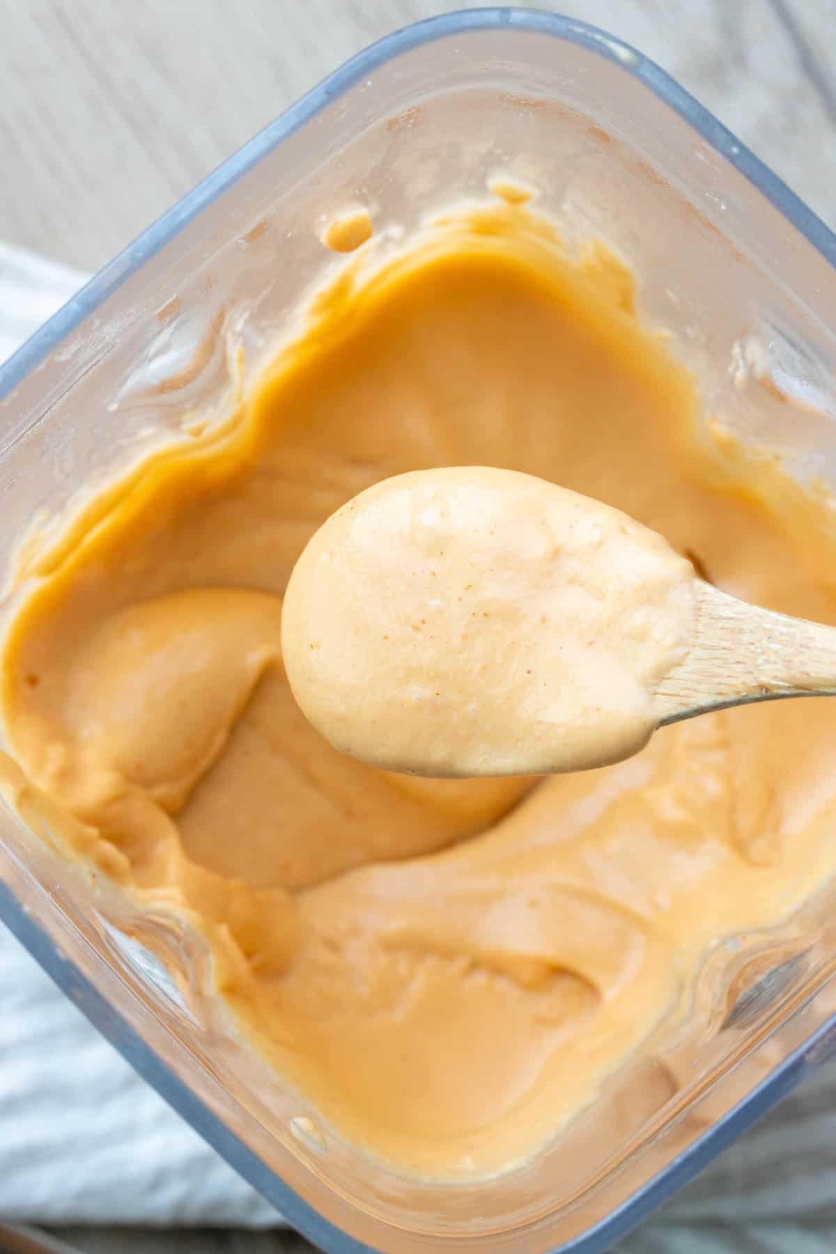 Spoon scooping orange cheese sauce out of white gravy boat