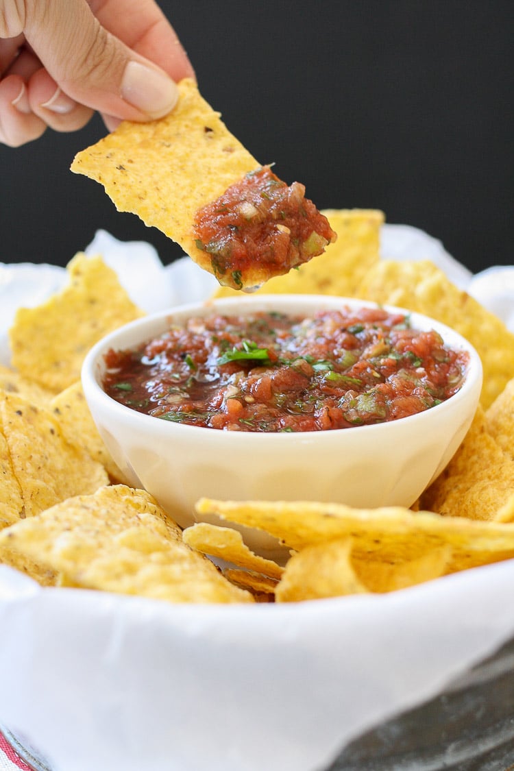 Hand dipping a tortilla chip into a white bowl of fresh Mexican salsa