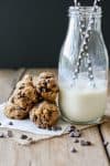 A small pile of Cookie Dough Balls next to a glass of milk with straws