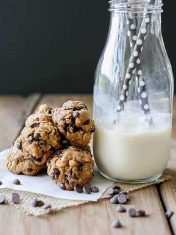 A small pile of Cookie Dough Balls‬‬‬‬‬‬‬‬‬‬‬ next to a glass of milk with straws