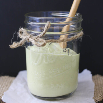 Glass jar with a spoon and half filled with green creamy dill sauce
