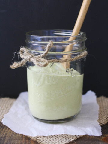 Glass jar with a spoon and half filled with green creamy dill sauce