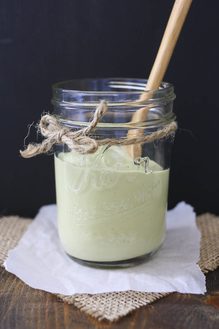 Glass jar with a spoon and half filled with green creamy dill sauce