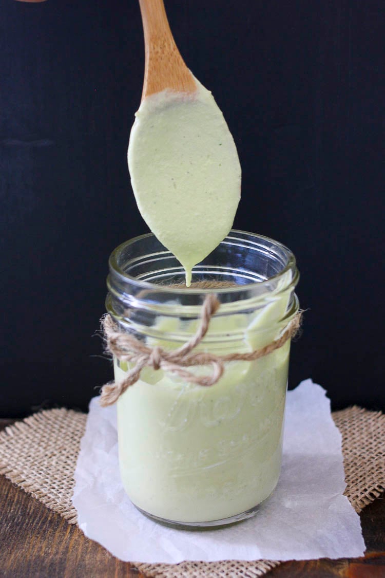 A wooden spoon coming out of a glass jar covered in creamy green dill sauce 